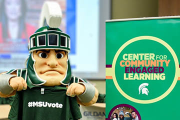 Mascot Sparty holding up MSUVote t-shirt