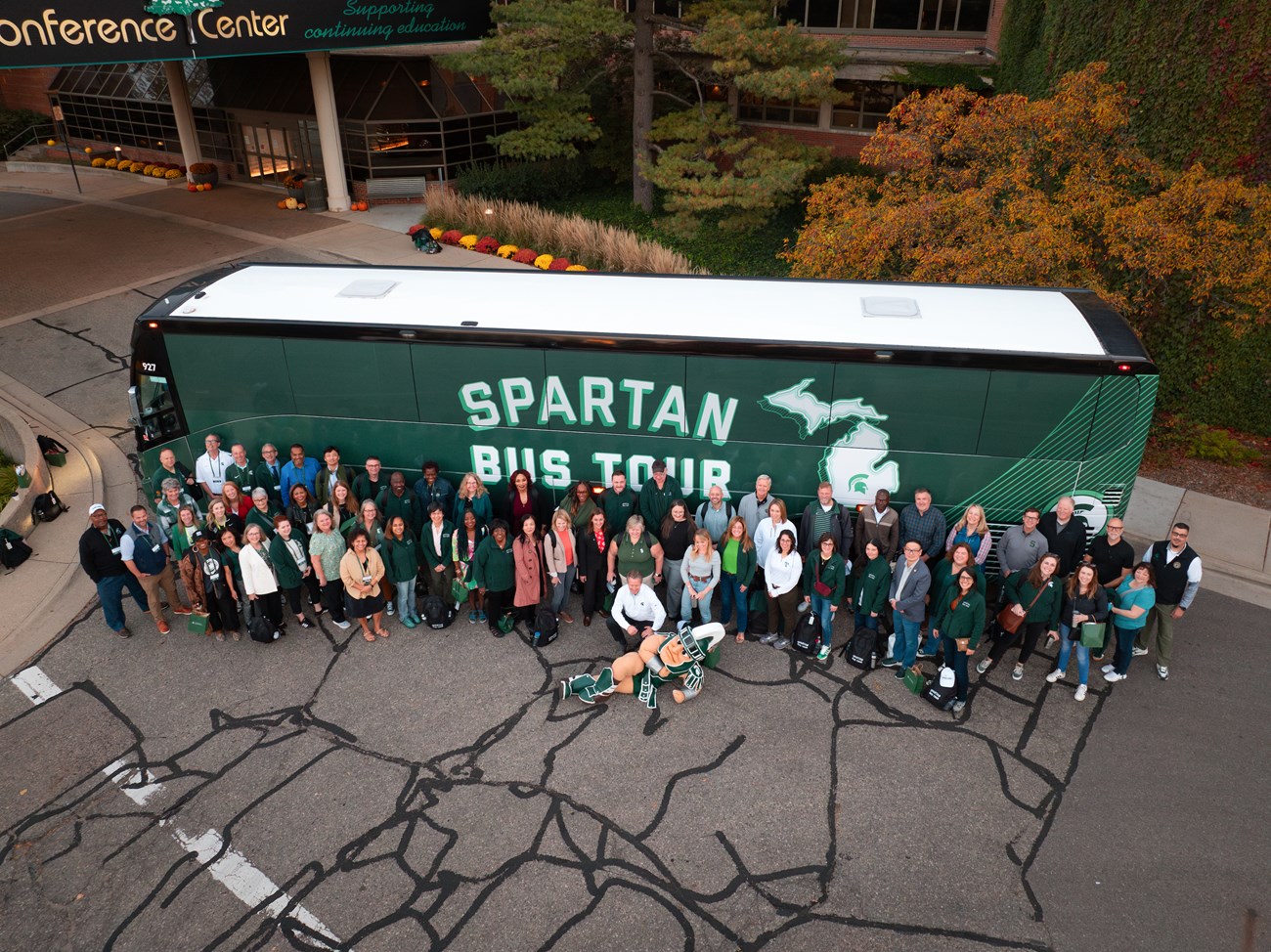 A group of MSU professionals stands alongside the Spartan Bus outside of the Kellogg Hotel & Conference Center