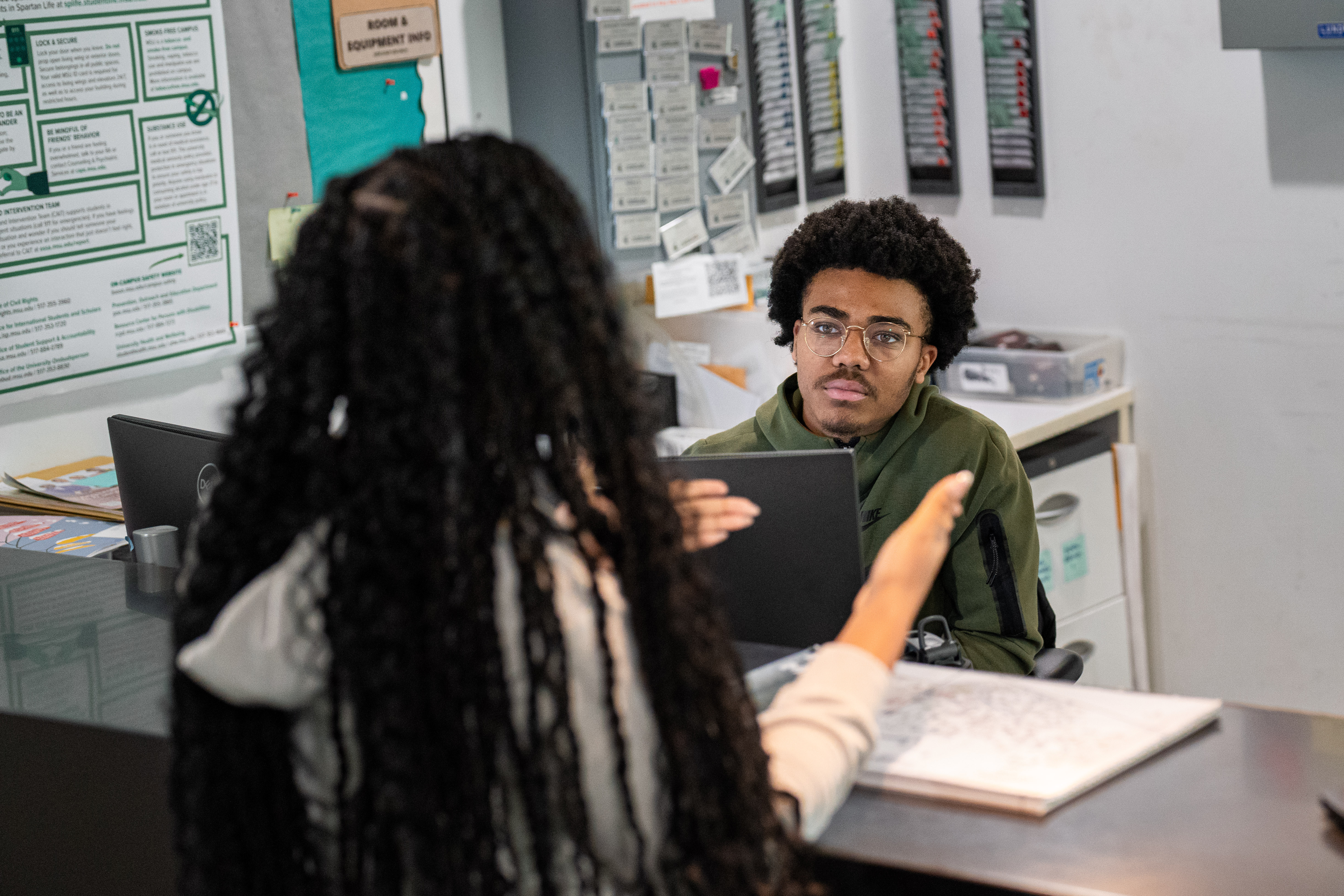 A student employee of the Brody Service Center assists another student at the Service Center desk.