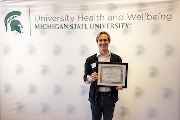 Robert Mueller stands, smiling and holding their Spirit of Ability Award at the reception held at the Kellogg Center