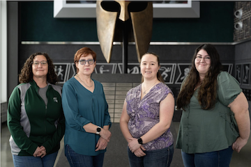 The core team of the Women in Facilities ERG, Cara Jackson, Tracey Ryan, Brittney Sprague and Heather Whitman, stand in front of the Spartan Helmet at 1855 Place.