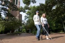 Blind student and companion walk around campus
