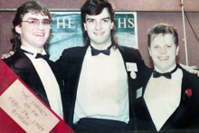 A vintage photo of three people dressed in formal attire, standing together and smiling. A ribbon in the corner reads 'THE IMPACT 89 FM FEB. 24, 1989 8:00 PM.