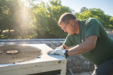 An SLE team member makes repairs while leaving over an outdoor air conditioning unit