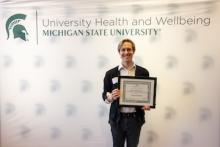 Robert Mueller stands, smiling and holding their Spirit of Ability Award at the reception held at the Kellogg Center