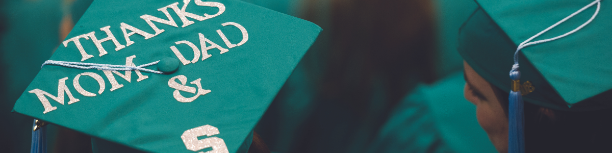 A graduation cap decorated with the words 'Thanks Mom, Dad & S' in glittery letters. The cap is worn by a graduate dressed in a green gown, with a tassel hanging from the cap.